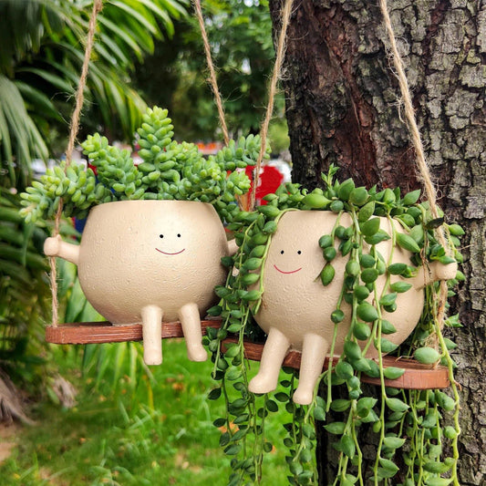 Deux pots suspendus à bout de bras assis sur une balançoire en bois, avec des plantes retombantes